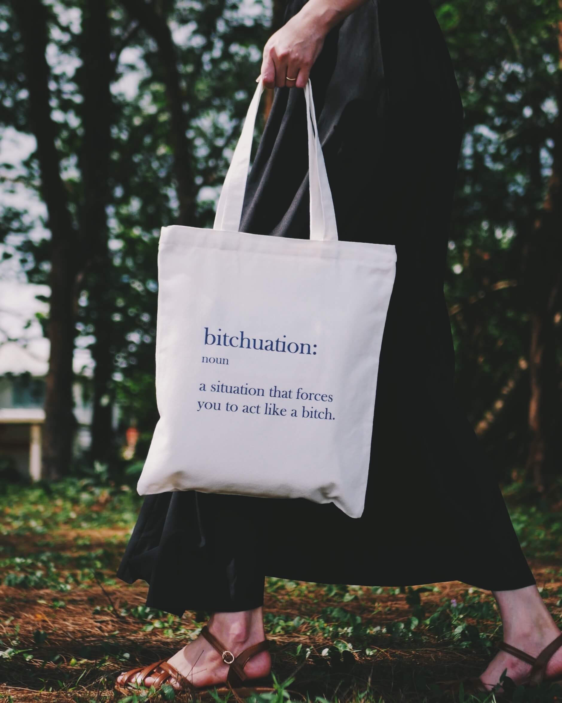 Person holding a 'bitchuation' tote bag in a forest setting