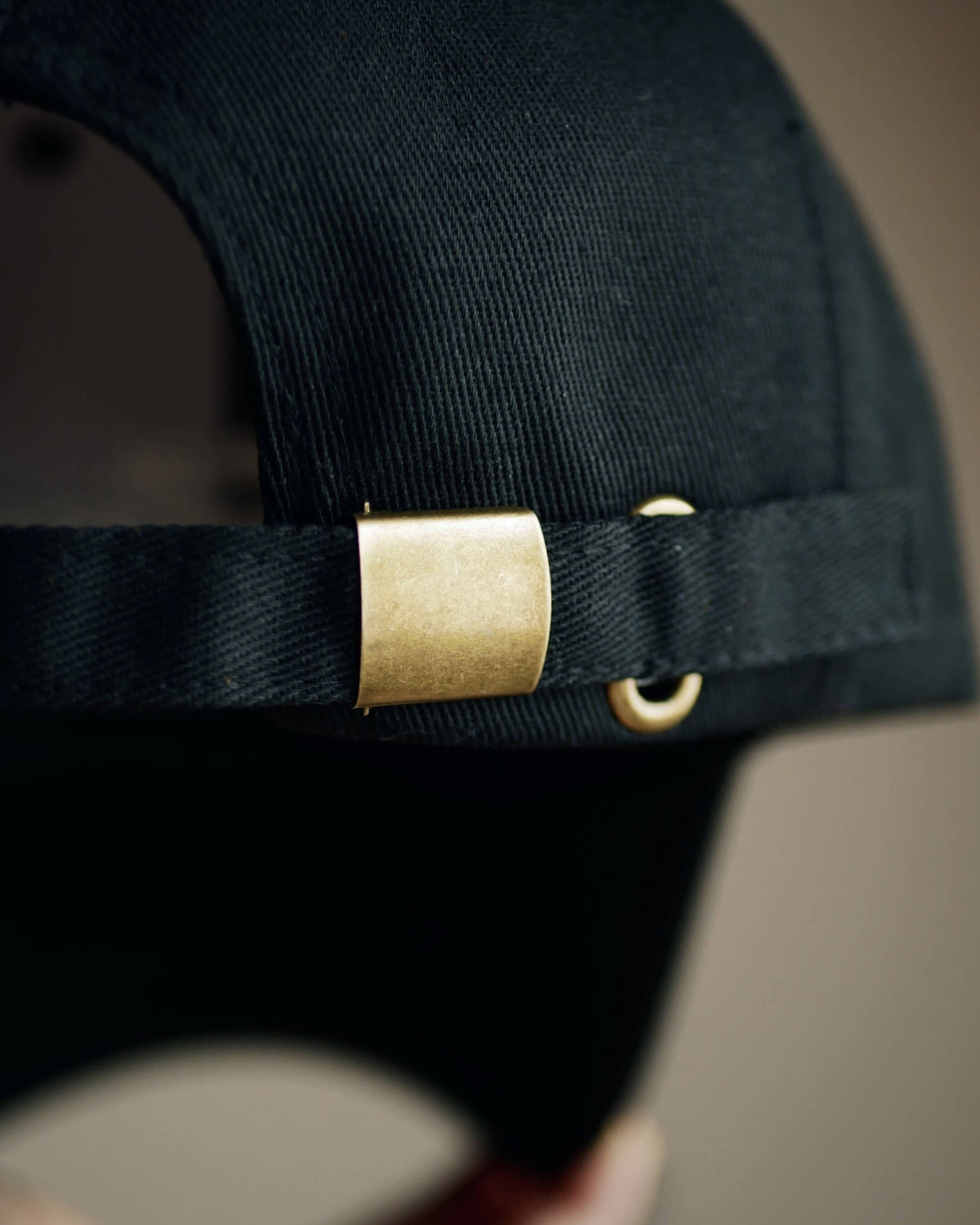 Close-up of a black canvas baseball cap with a brass metal buckle strap adjustment.