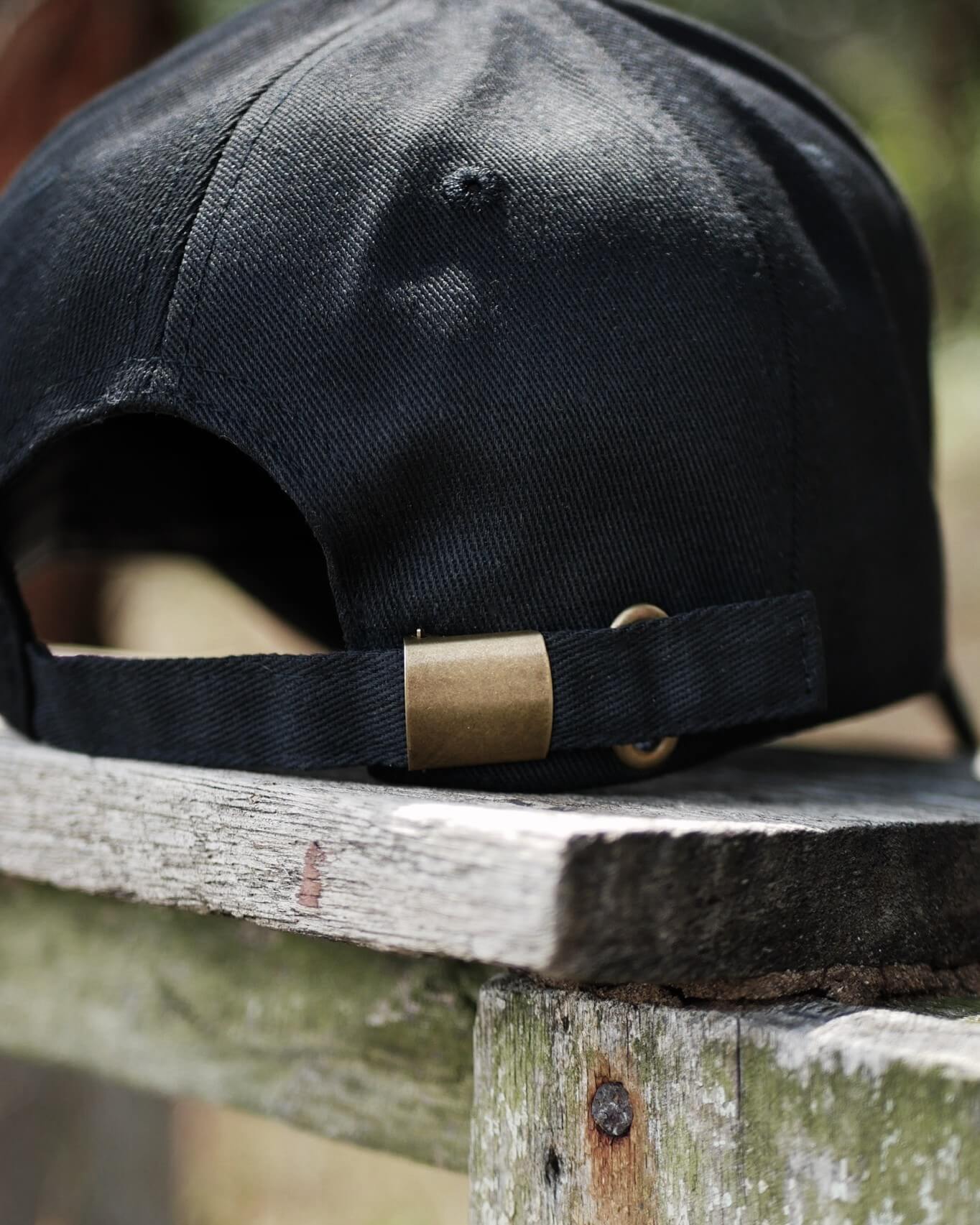 Black cap with a gold buckle on a wooden surface outdoors