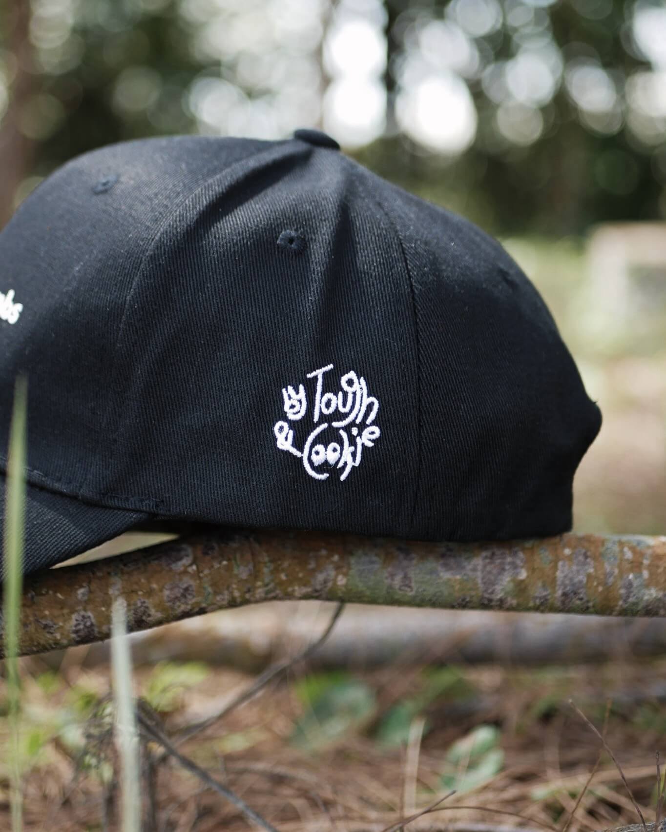 Black cap with white logo on a branch outdoors