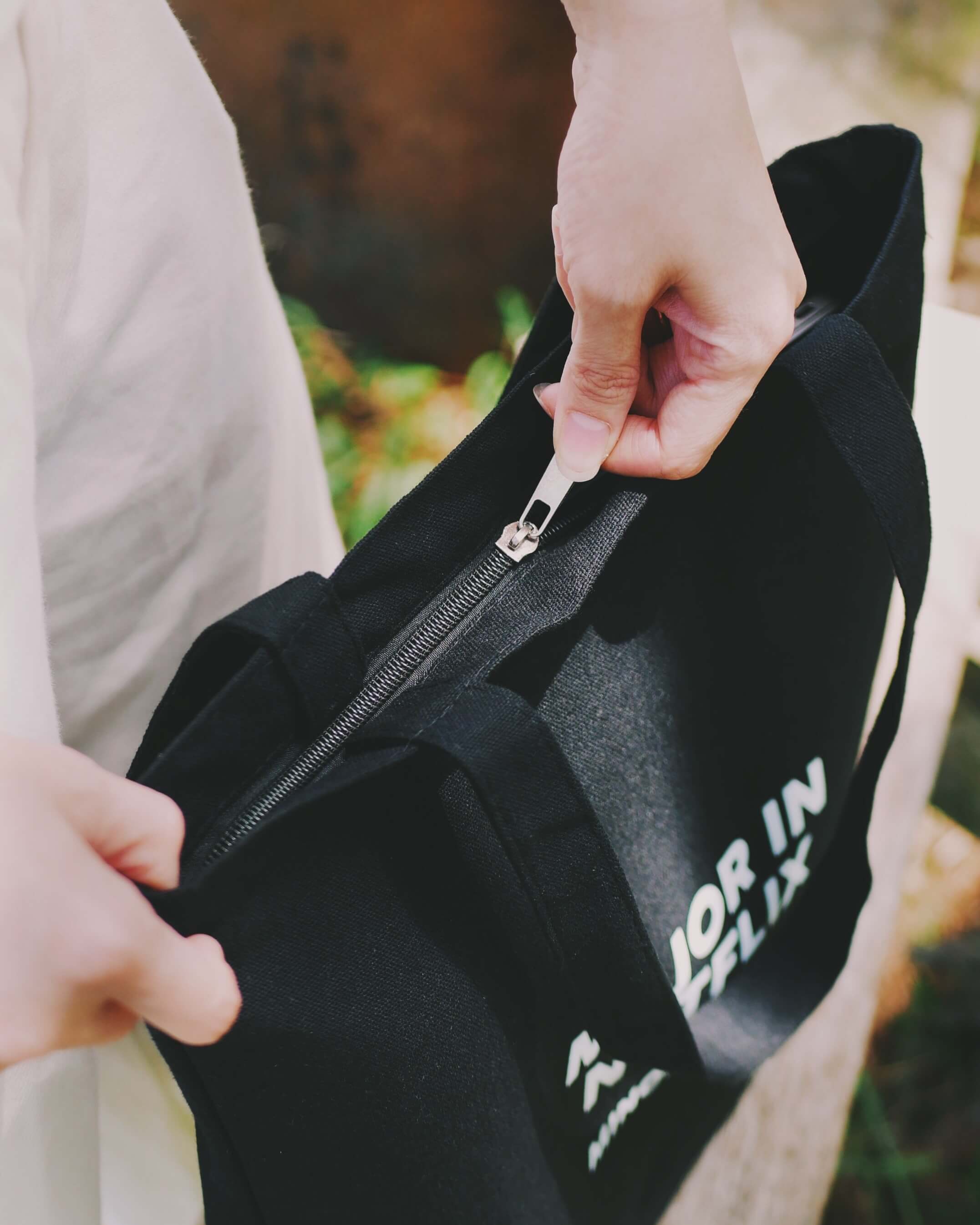 Person zipping a black tote bag outdoors