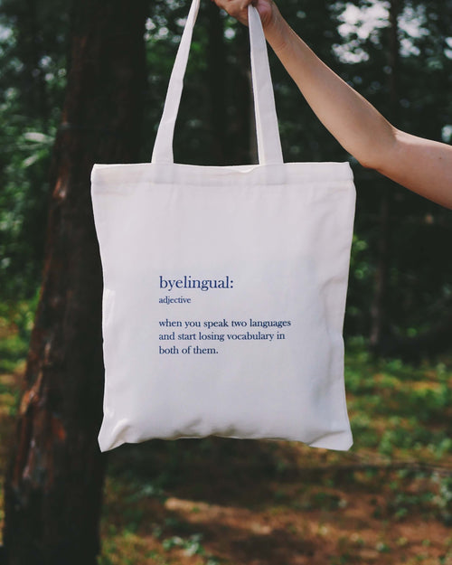 Tote bag with a definition of 'byelingual' held by a person outdoors.