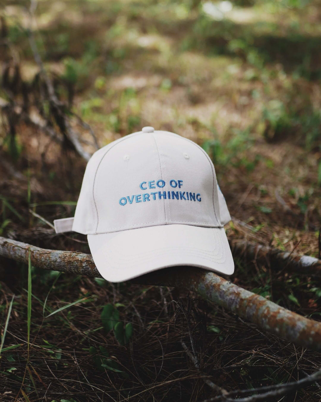 White cap with 'CEO of Overthinking' text on a branch in a natural setting