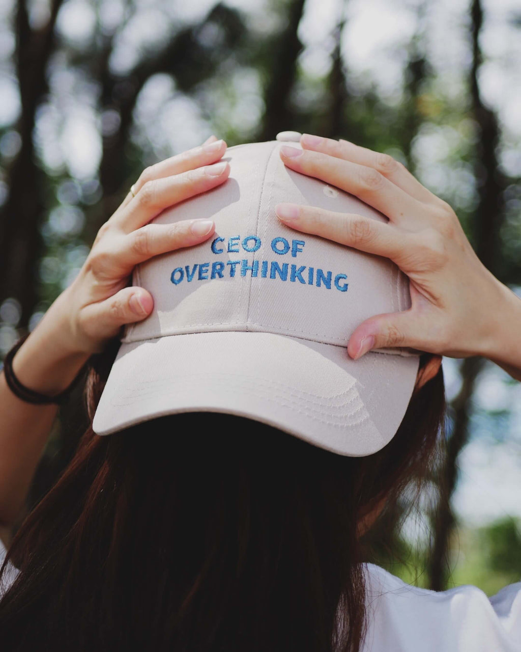 Person wearing a cap with 'CEO of Overthinking' text against a blurred natural background