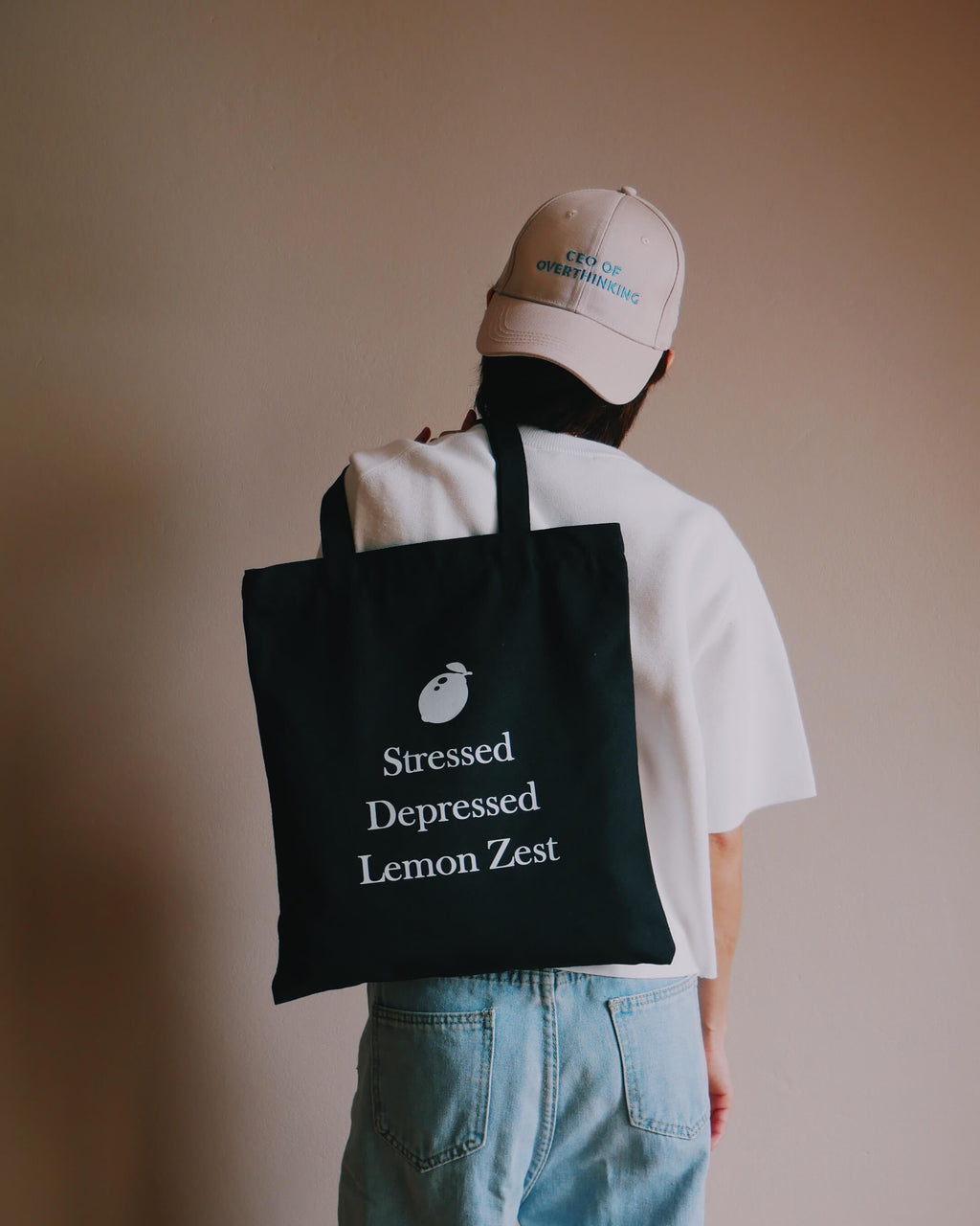 Person wearing a creap cap and black tote bag with text, standing against a plain background
