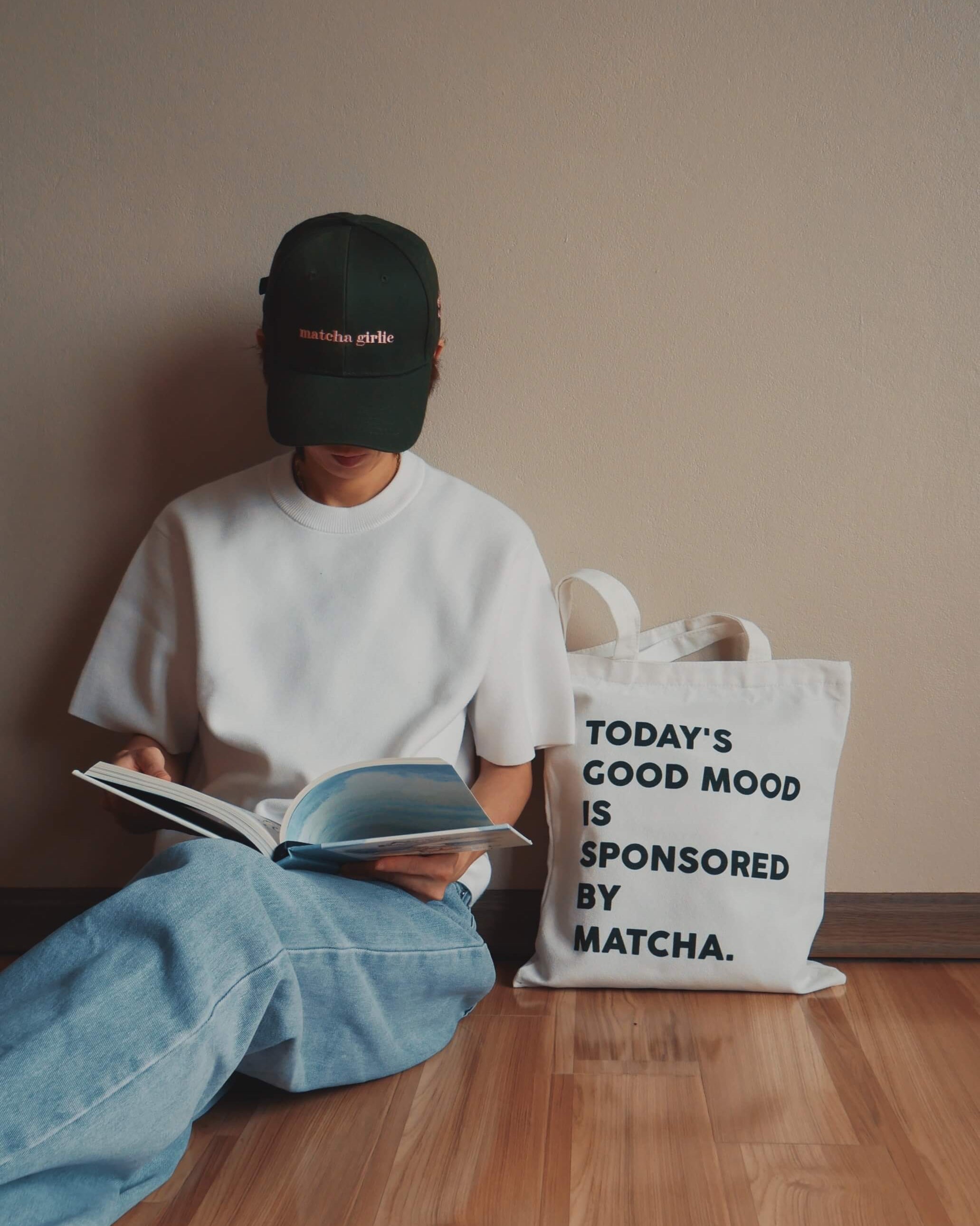 Person sitting on the floor reading a book with a 'Matcha' bag next to them.