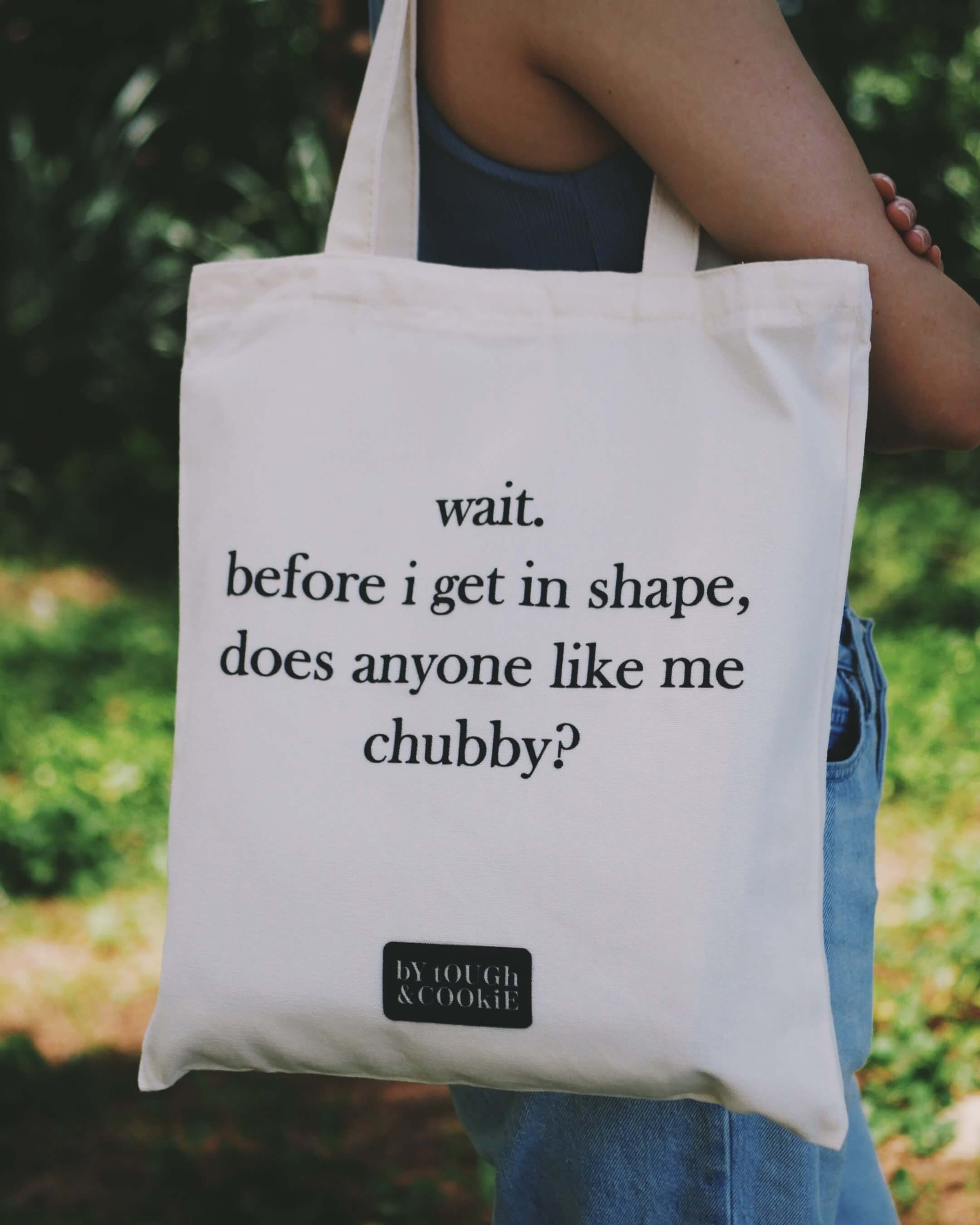 Tote bag with humorous text about getting in shape held by a person outdoors