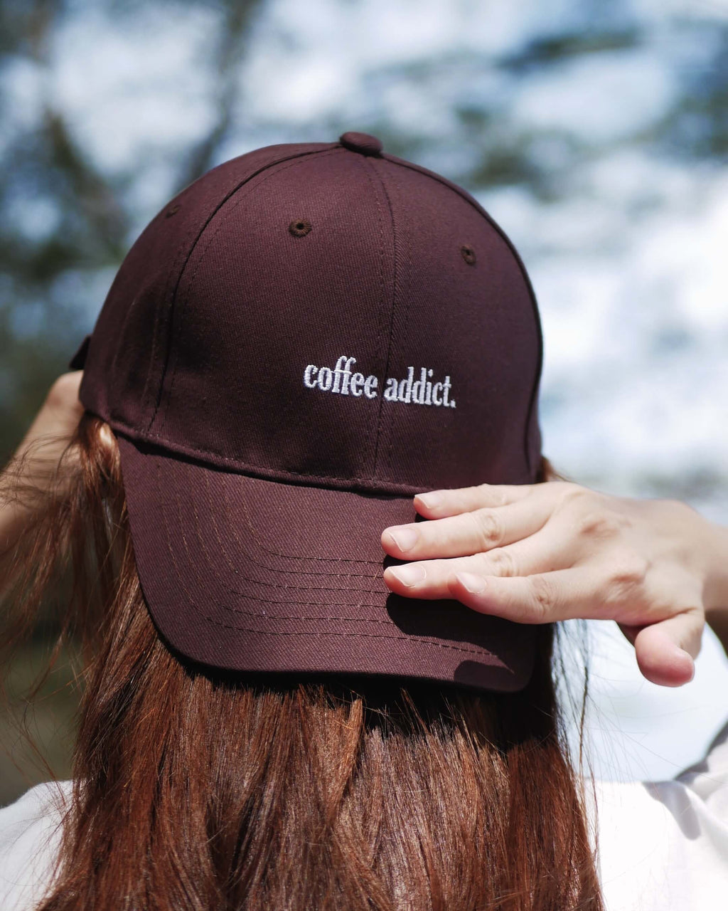 Brown cap with 'coffee addict' text worn by a person outdoors