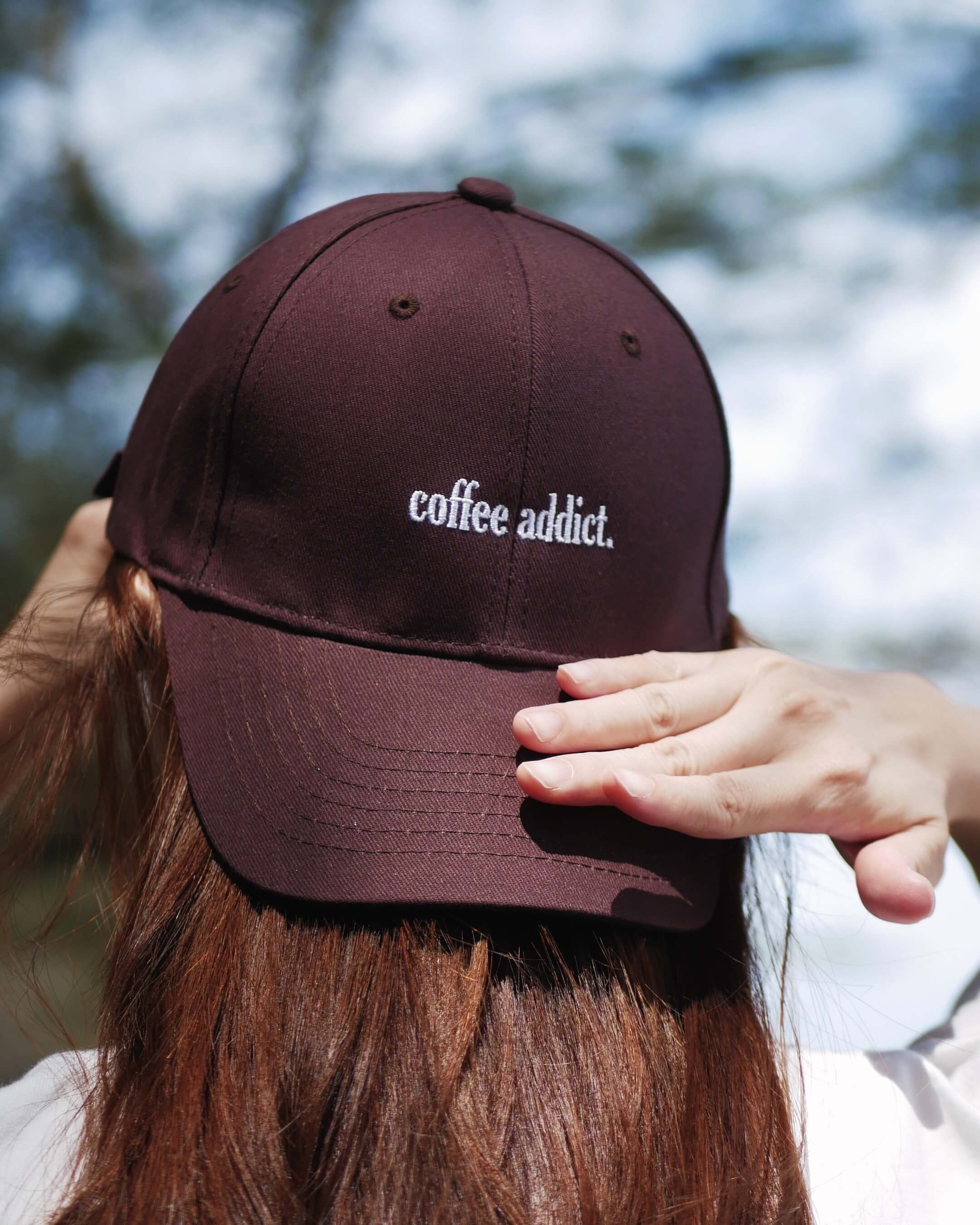 Brown cap with 'coffee addict' text worn by a person outdoors