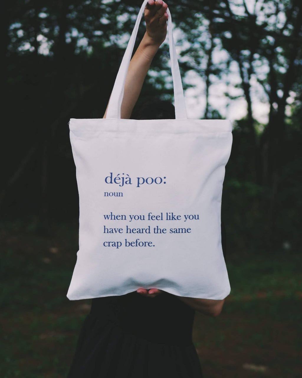 A person holding up a "Deja Poo" tote bag outdoor