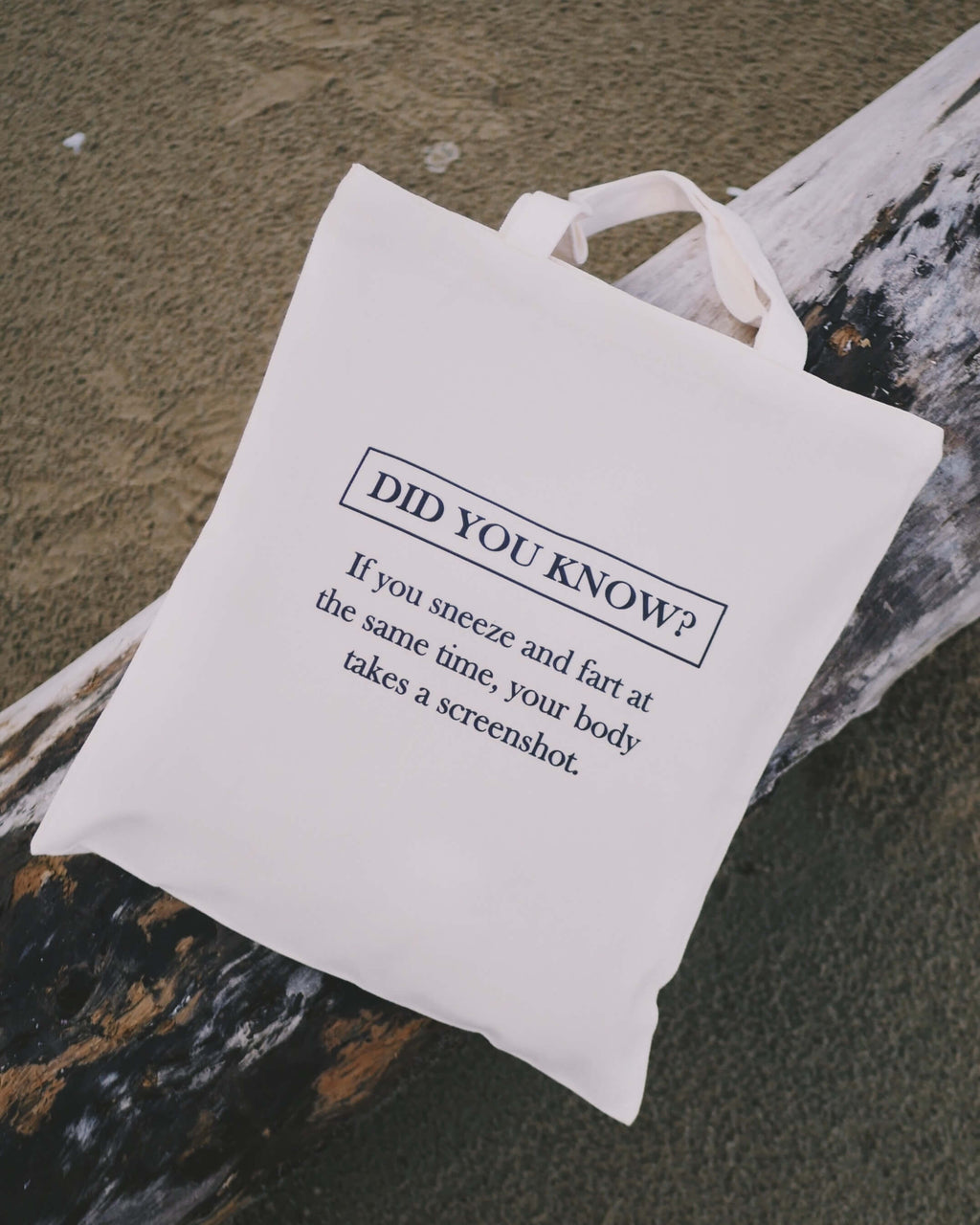 White tote bag with humorous text on a wooden surface at the beach