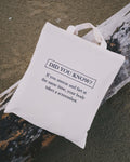 White tote bag with humorous text on a wooden surface at the beach