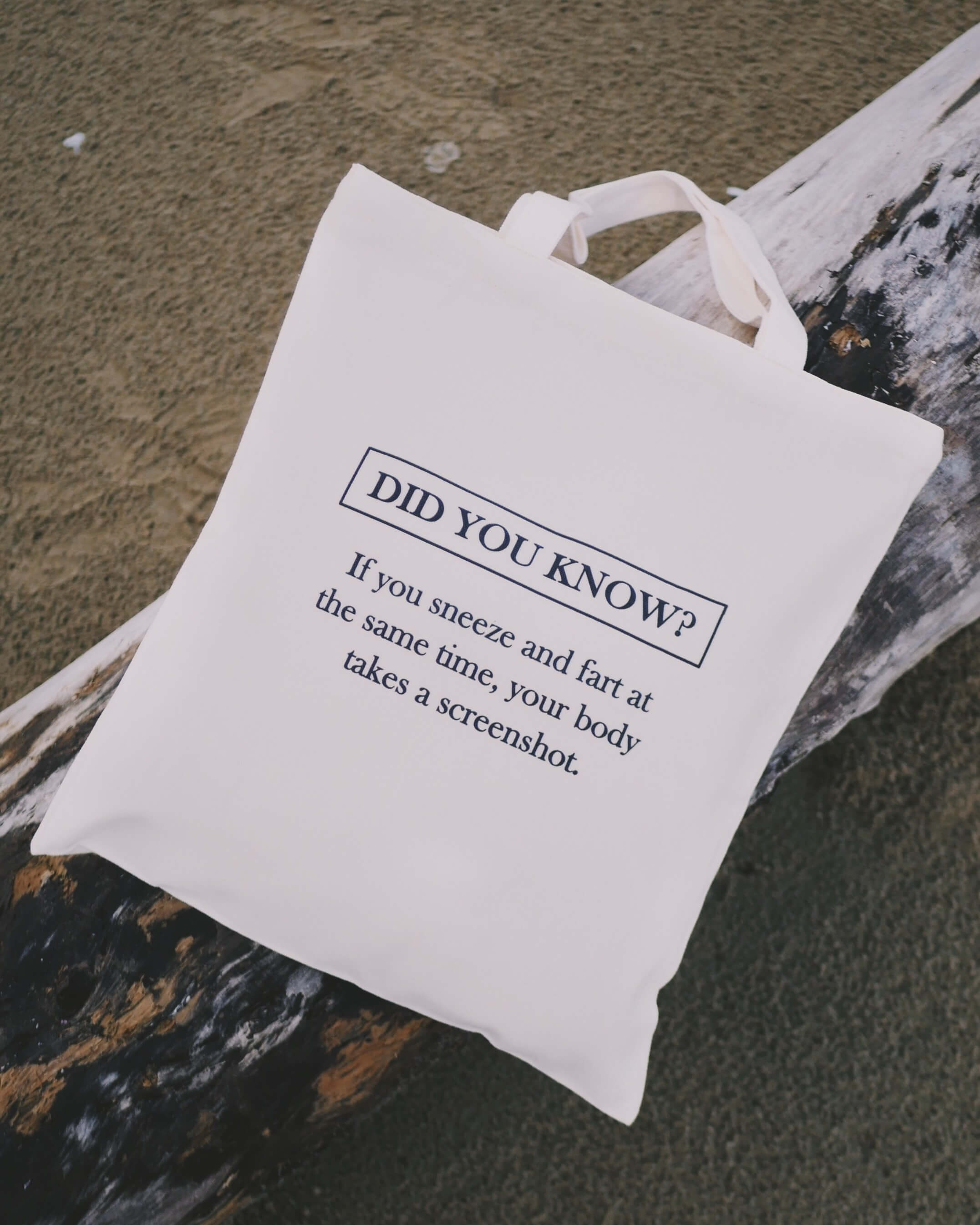 White tote bag with humorous text on a wooden surface at the beach
