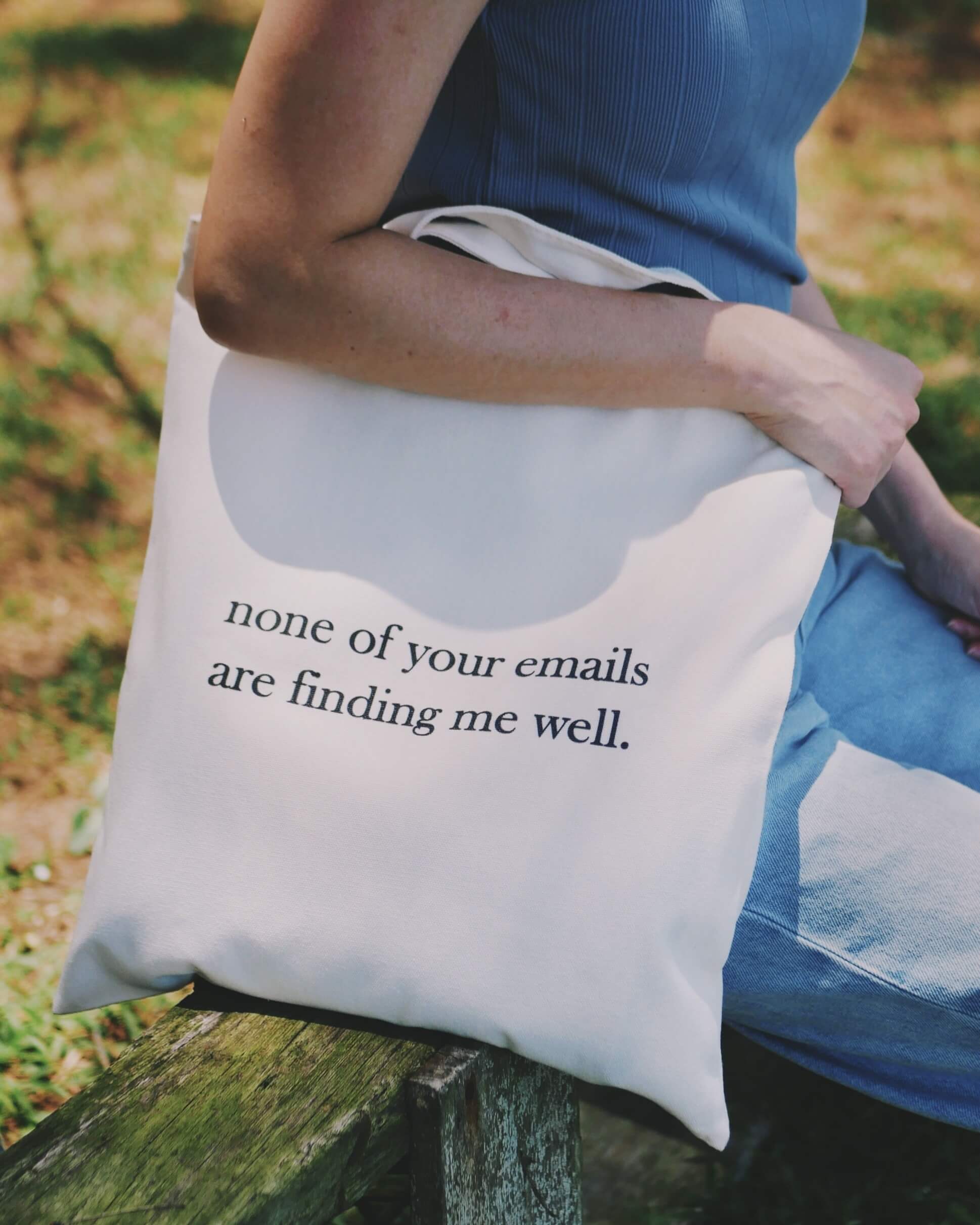 Person holding a tote bag with text 'none of your emails are finding me well.'