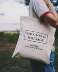 Tote bag with 'EMOTIONAL BAGGAGE' text held by a person outdoors.