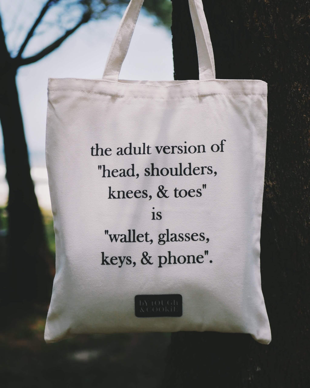 Tote bag with humorous text about adult essentials hanging on a tree