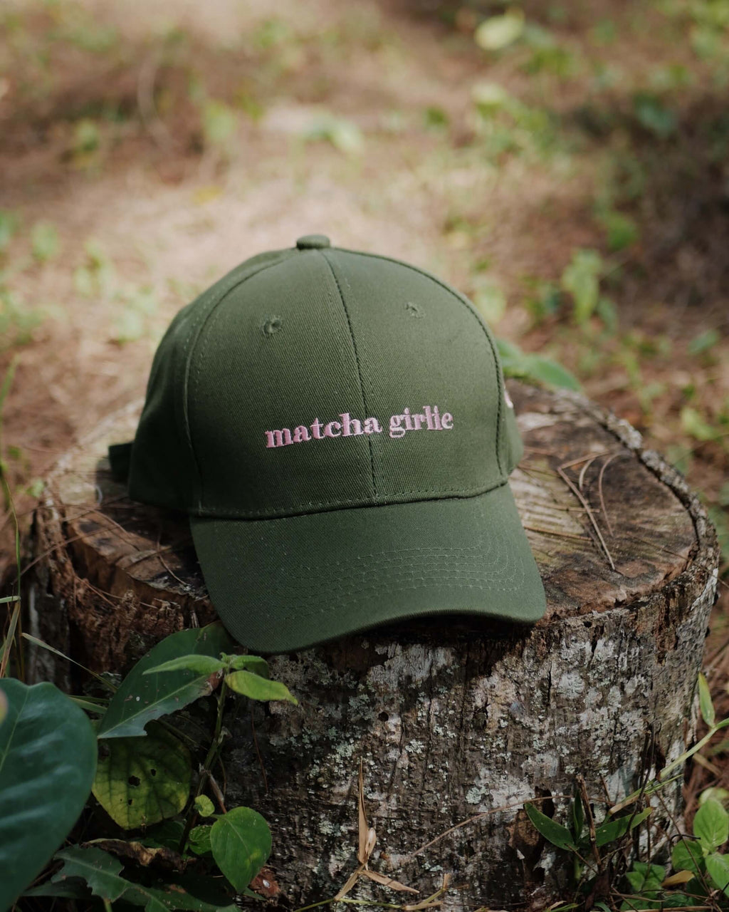 Green cap with 'matcha girlie' text on a wooden stump in a natural setting