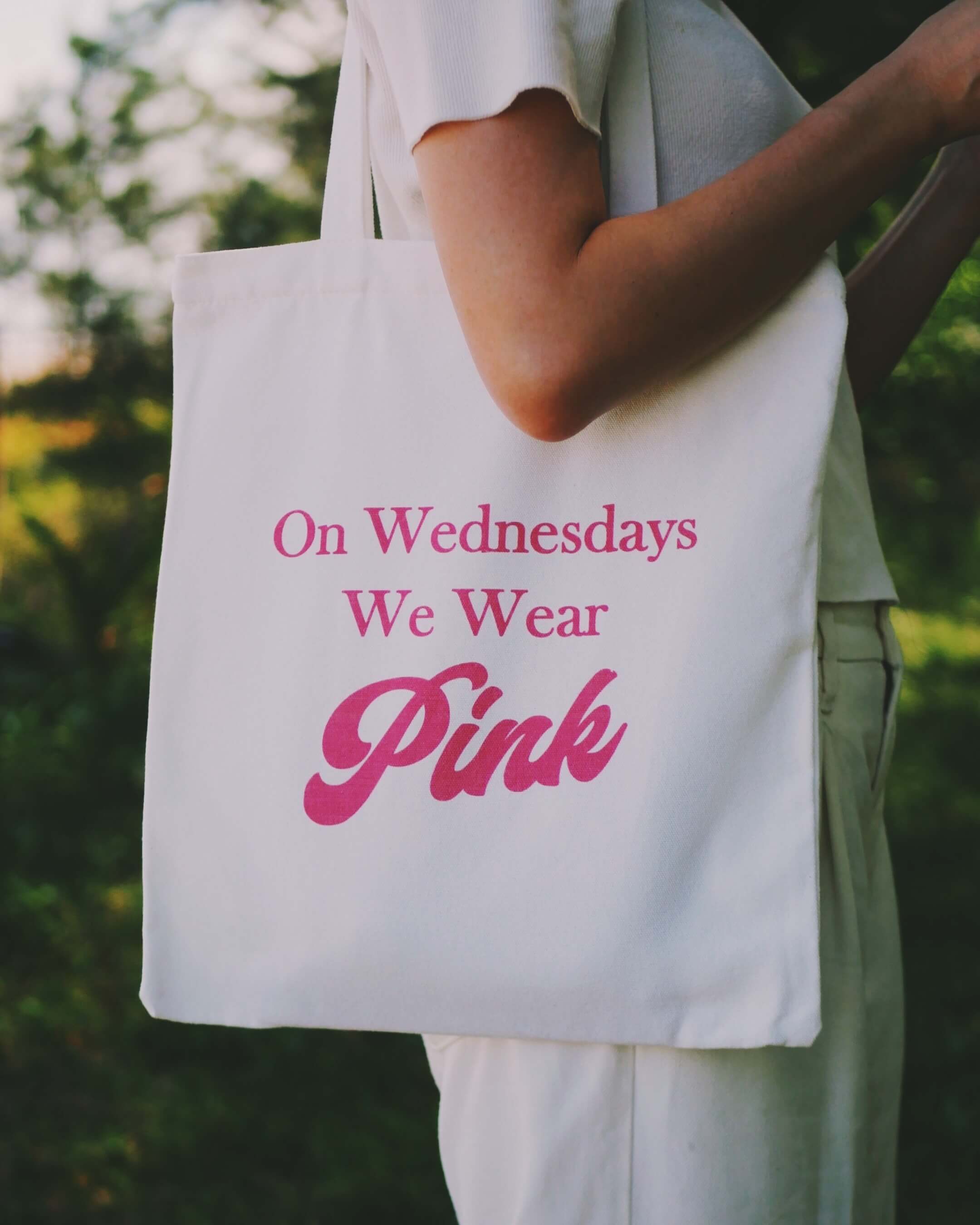 Person holding a tote bag with 'On Wednesdays We Wear Pink' text.