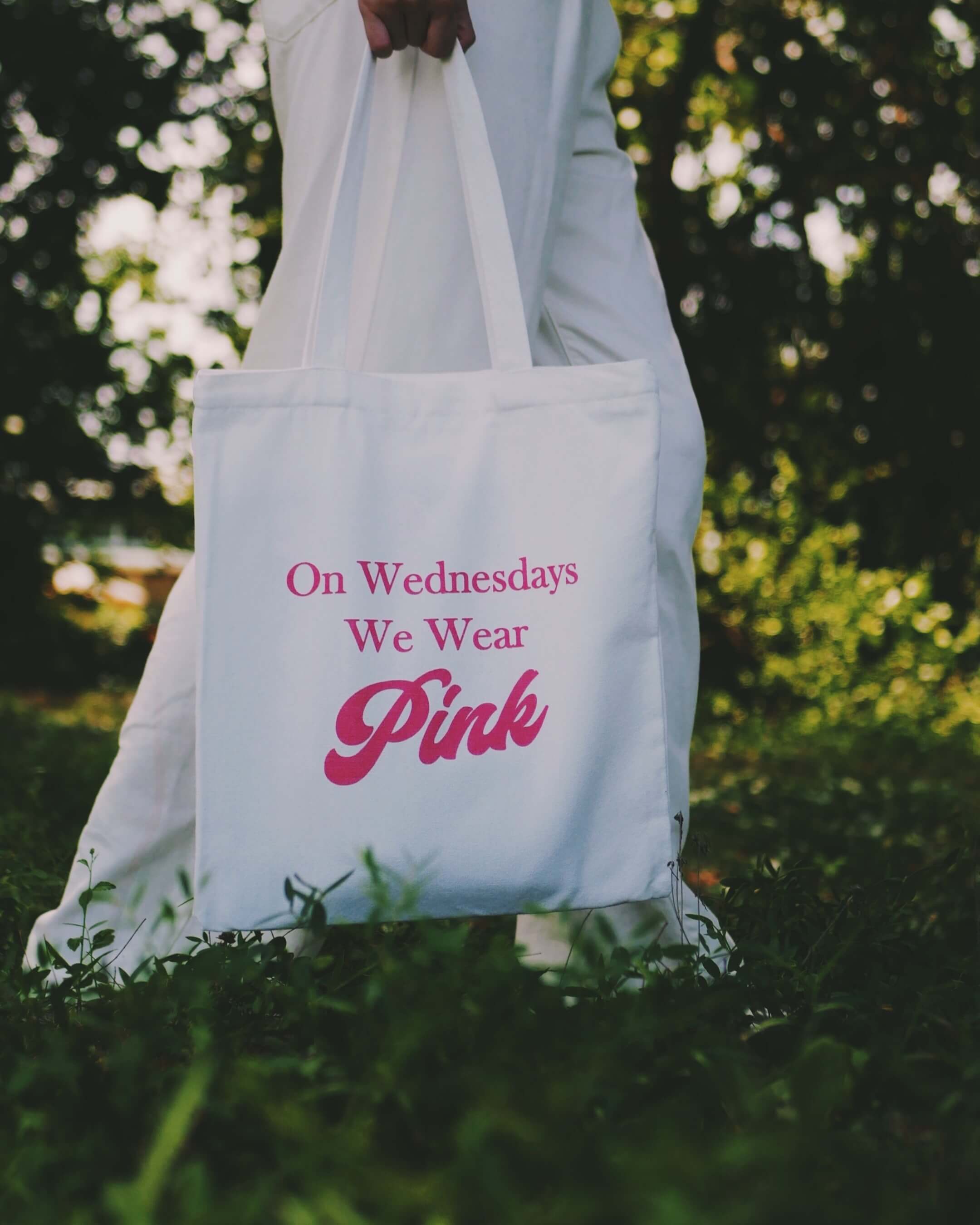 Tote bag with 'On Wednesdays We Wear Pink' text held by a person in a natural setting.