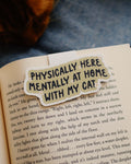 Magnetic bookmark with 'Physically here, mentally with my cat' design clipped on an open book.