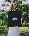 Person holding a black tote bag with 'Major in Netflix, Minor in Naps' text in a forest setting
