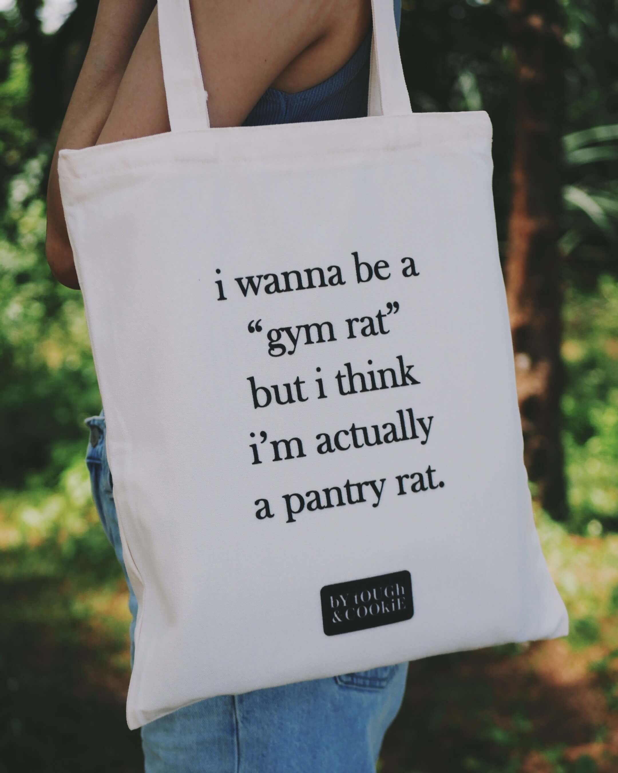 Tote bag with humorous text about bring a gym rat and pantry rat held by a person outdoors