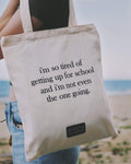 A person carrying a tote bag with humorous text on a beach.