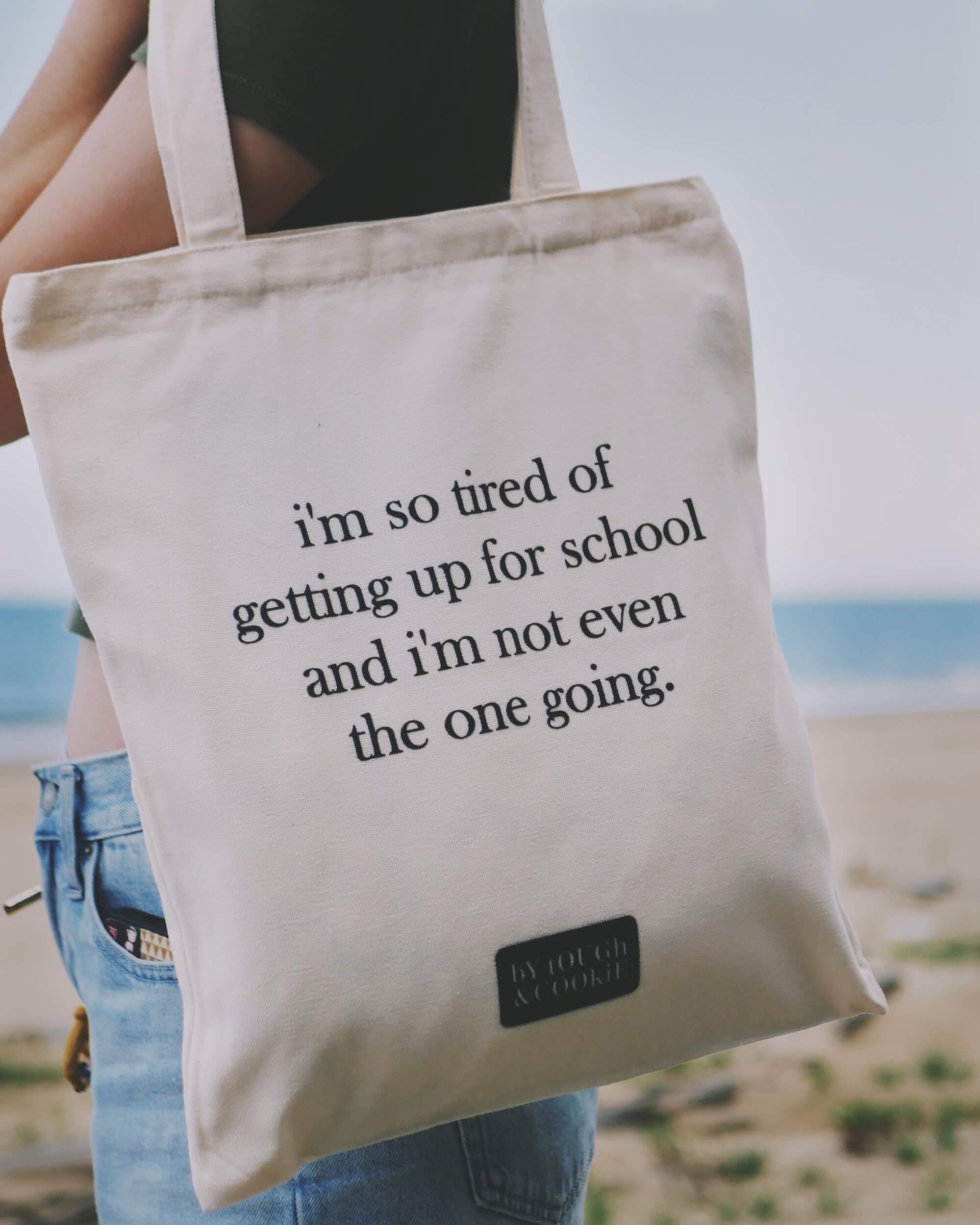 A person carrying a tote bag with humorous text on a beach.