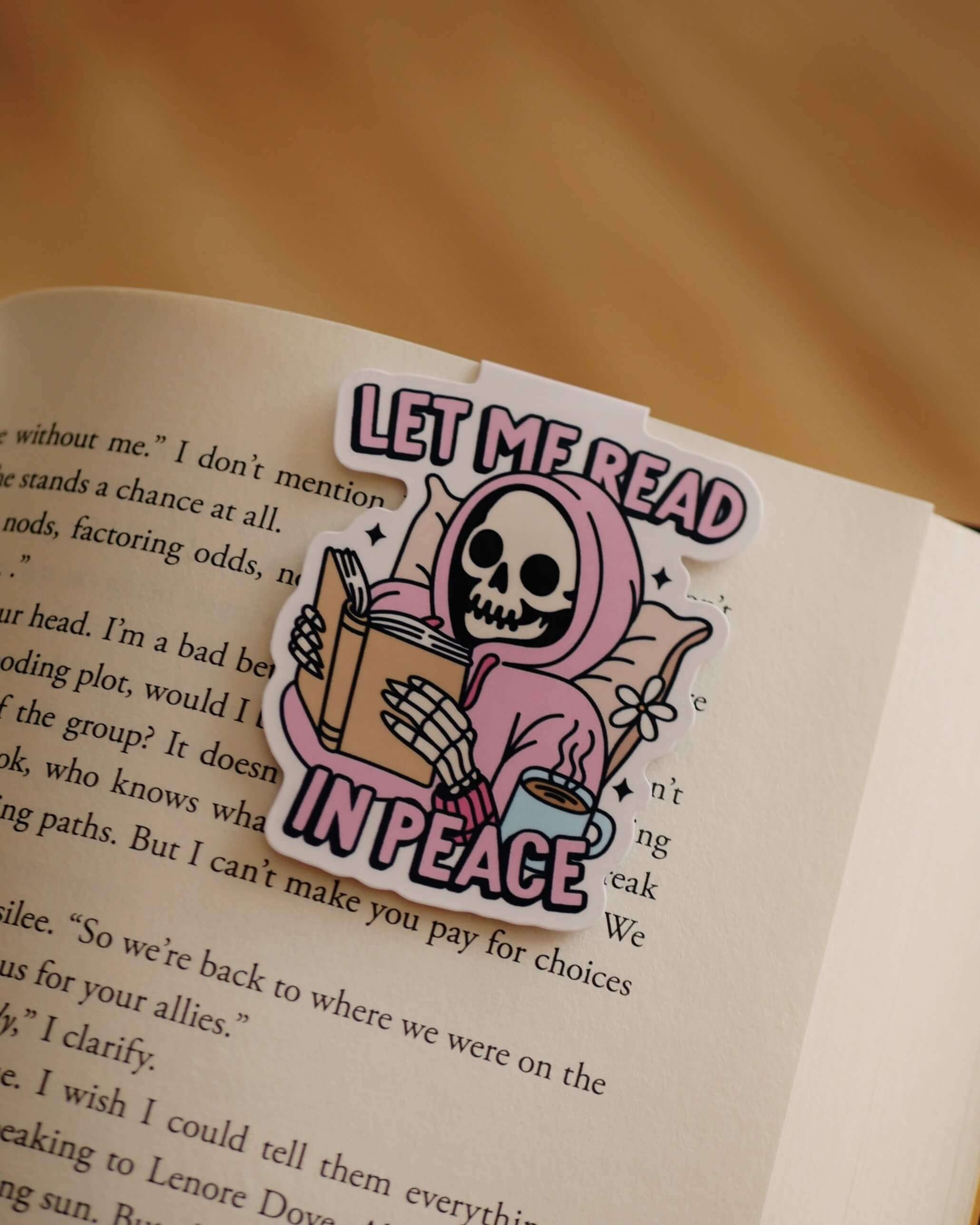 Magnetic bookmark with "Let Me Read In Peace" design clipped on an open book.