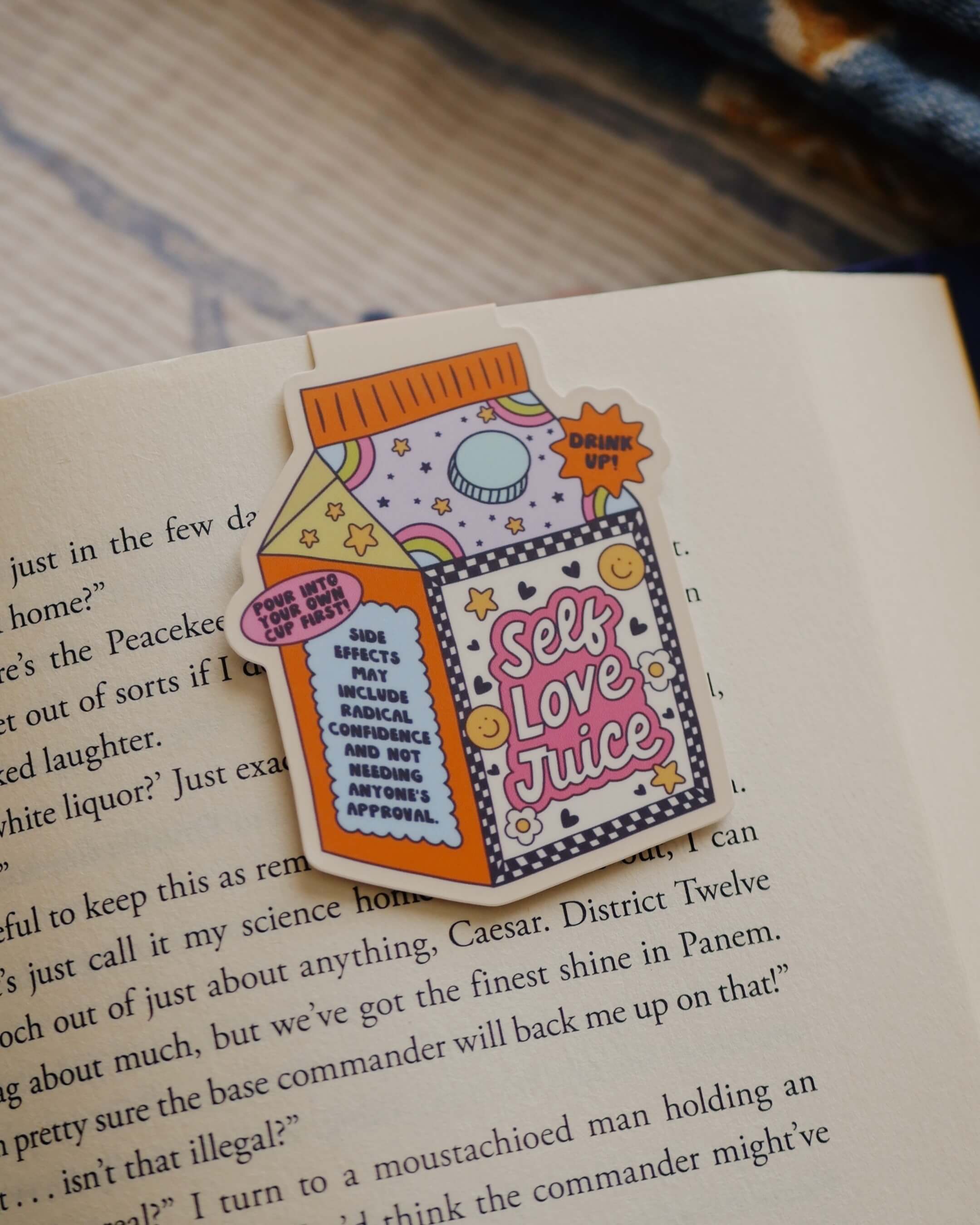 Magnetic bookmark with 'Self Love Juice' design clipped on an open book.