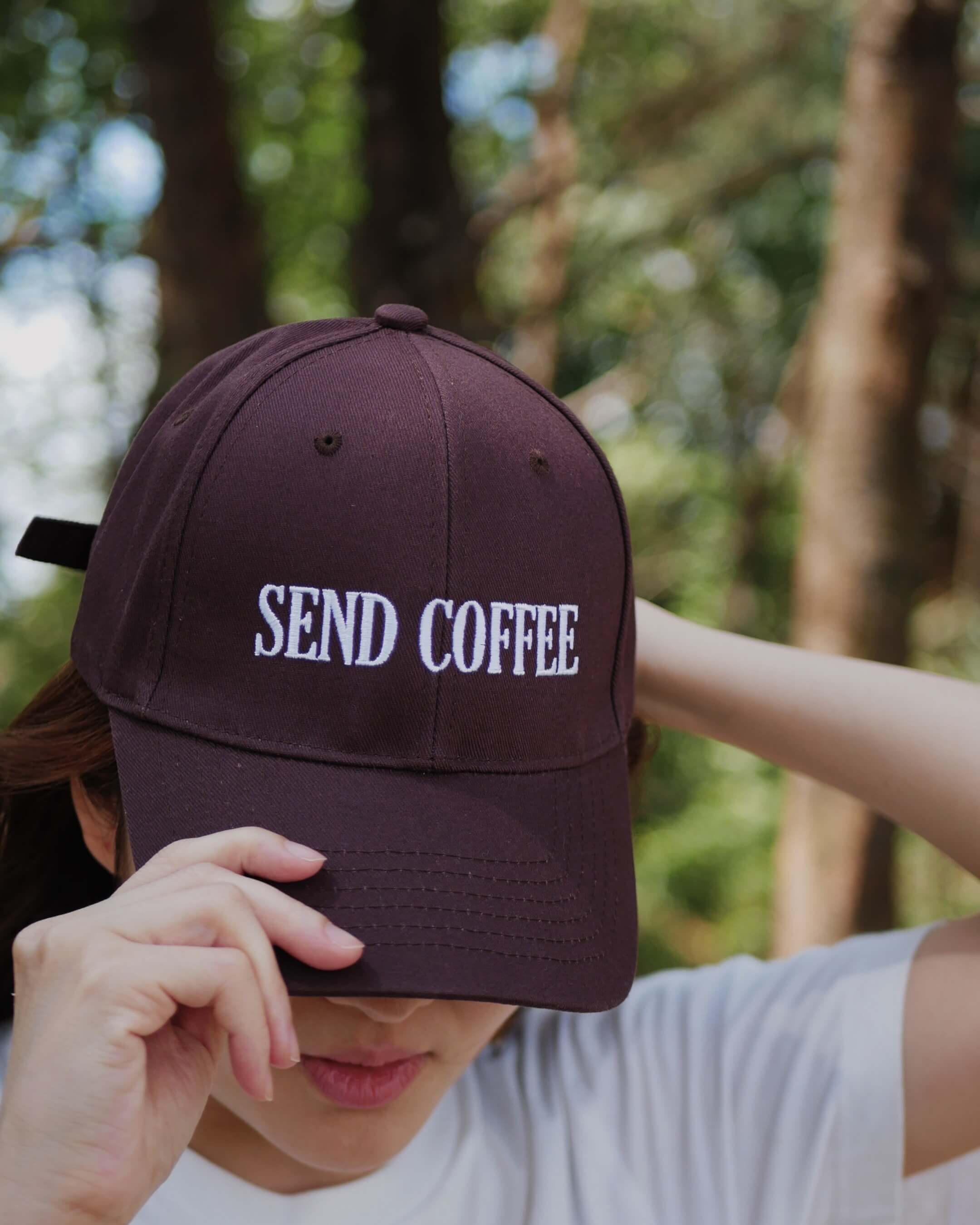 Person wearing a brown cap with 'SEND COFFEE' text in a forest setting