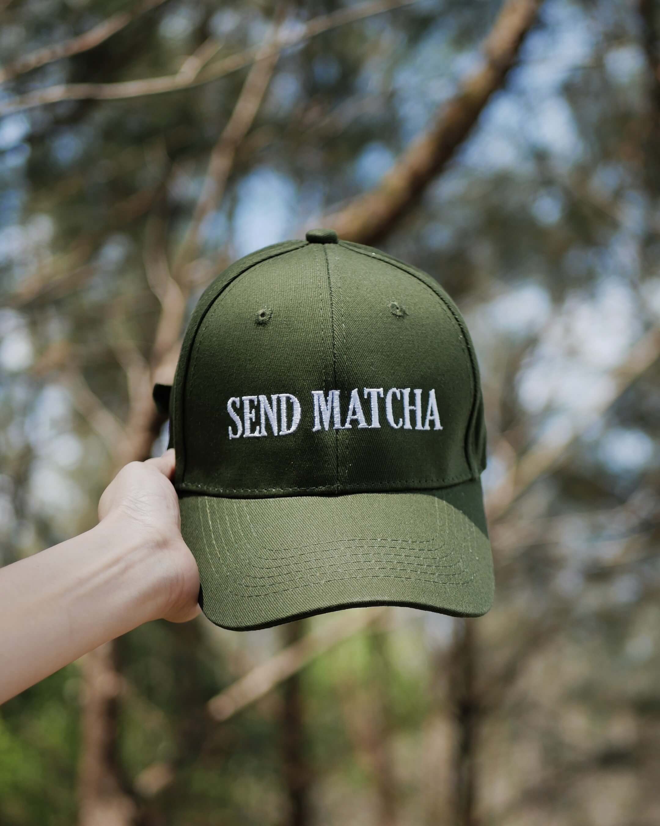 Green cap with 'SEND MATCHA' text held against a blurred natural background