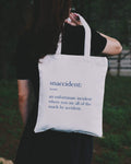 A person holding a 'Snaccident' tote bag outdoor
