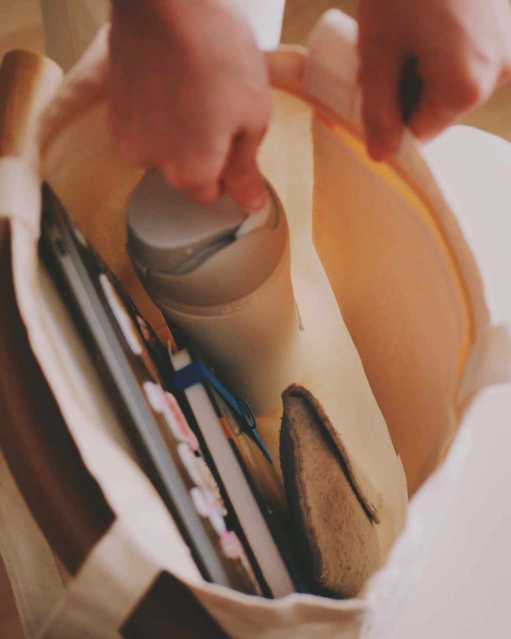 Person removing a thermo flask from a white tote bag.