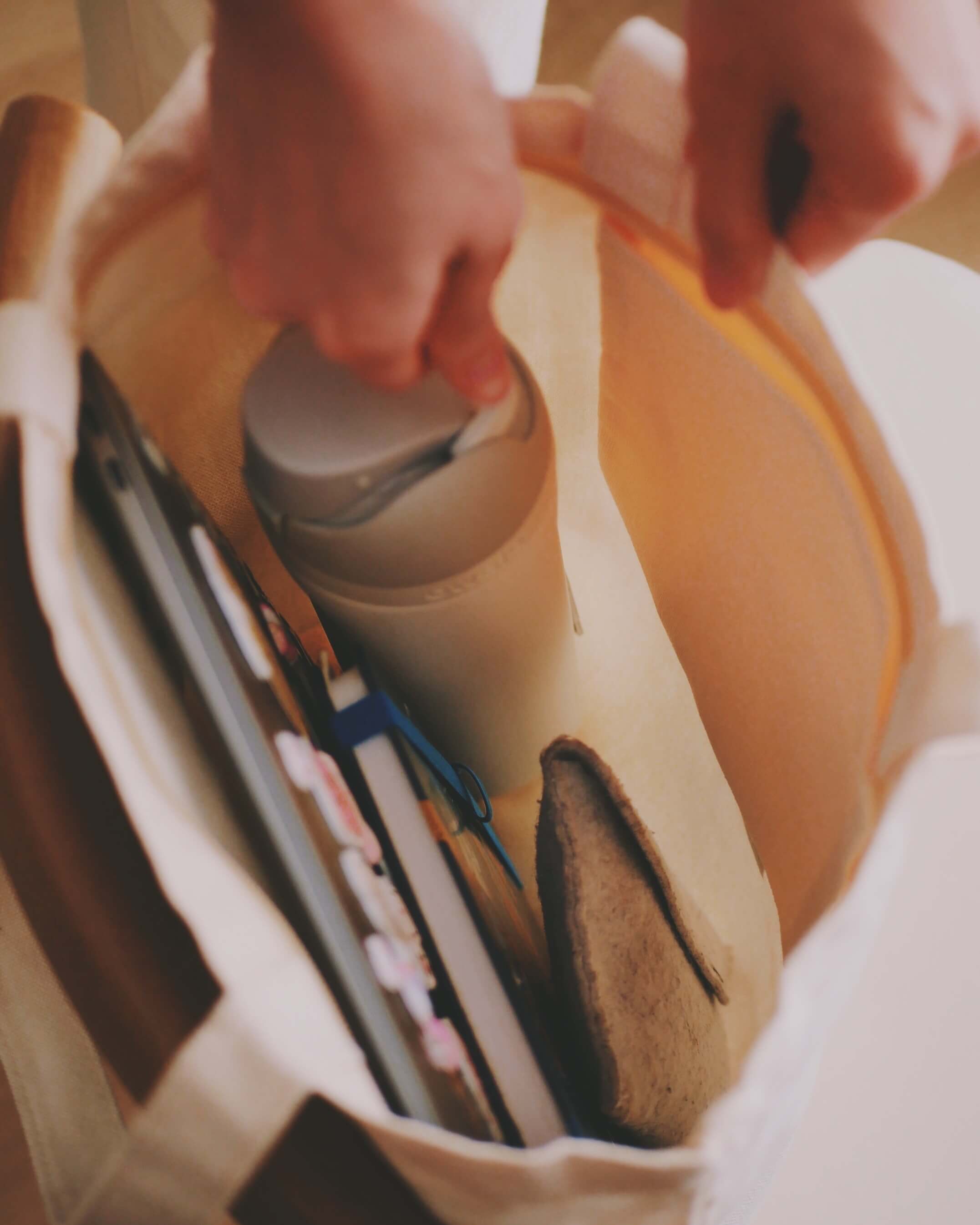 Person removing a thermo flask from a white tote bag.