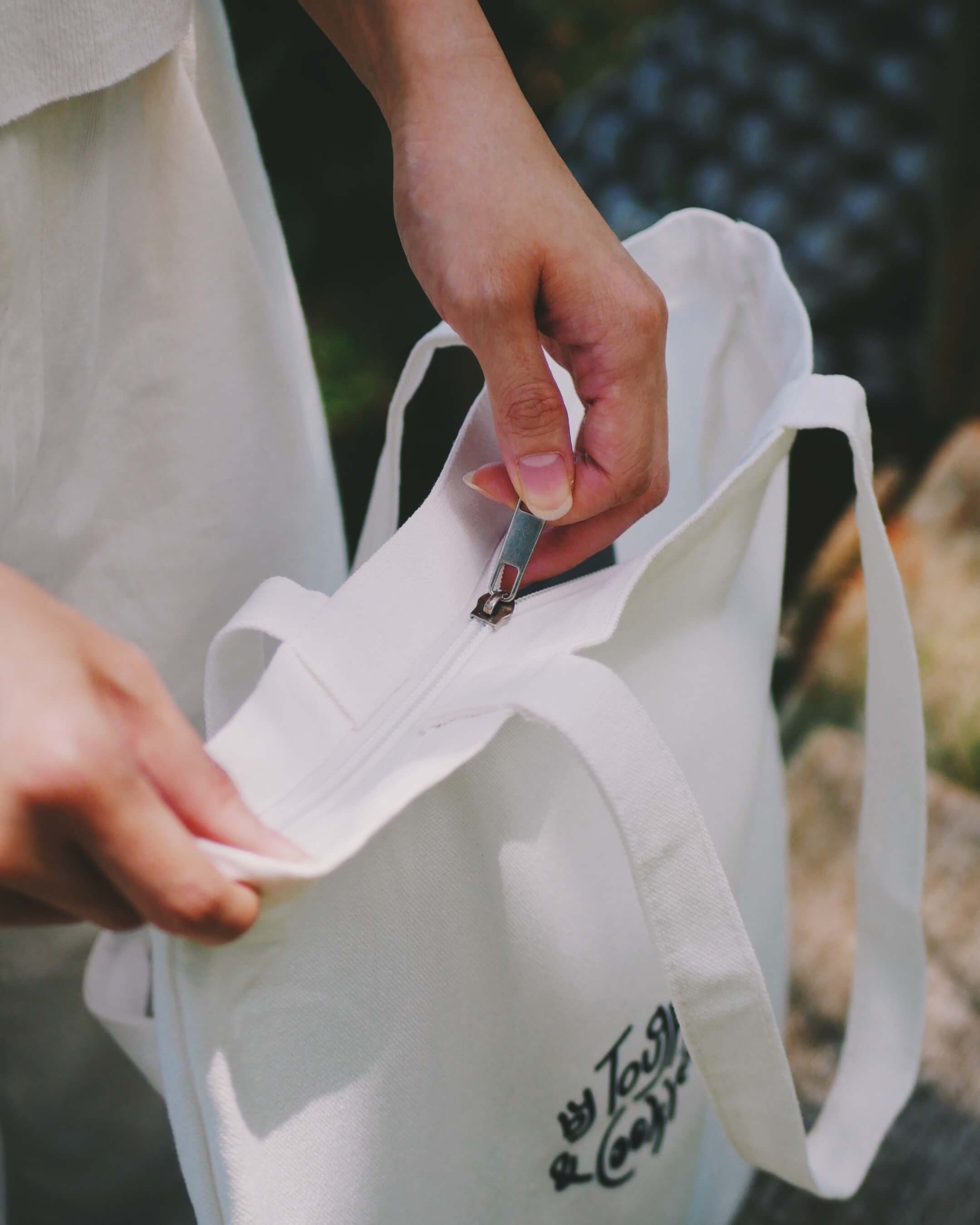 Person zipping a white tote bag
