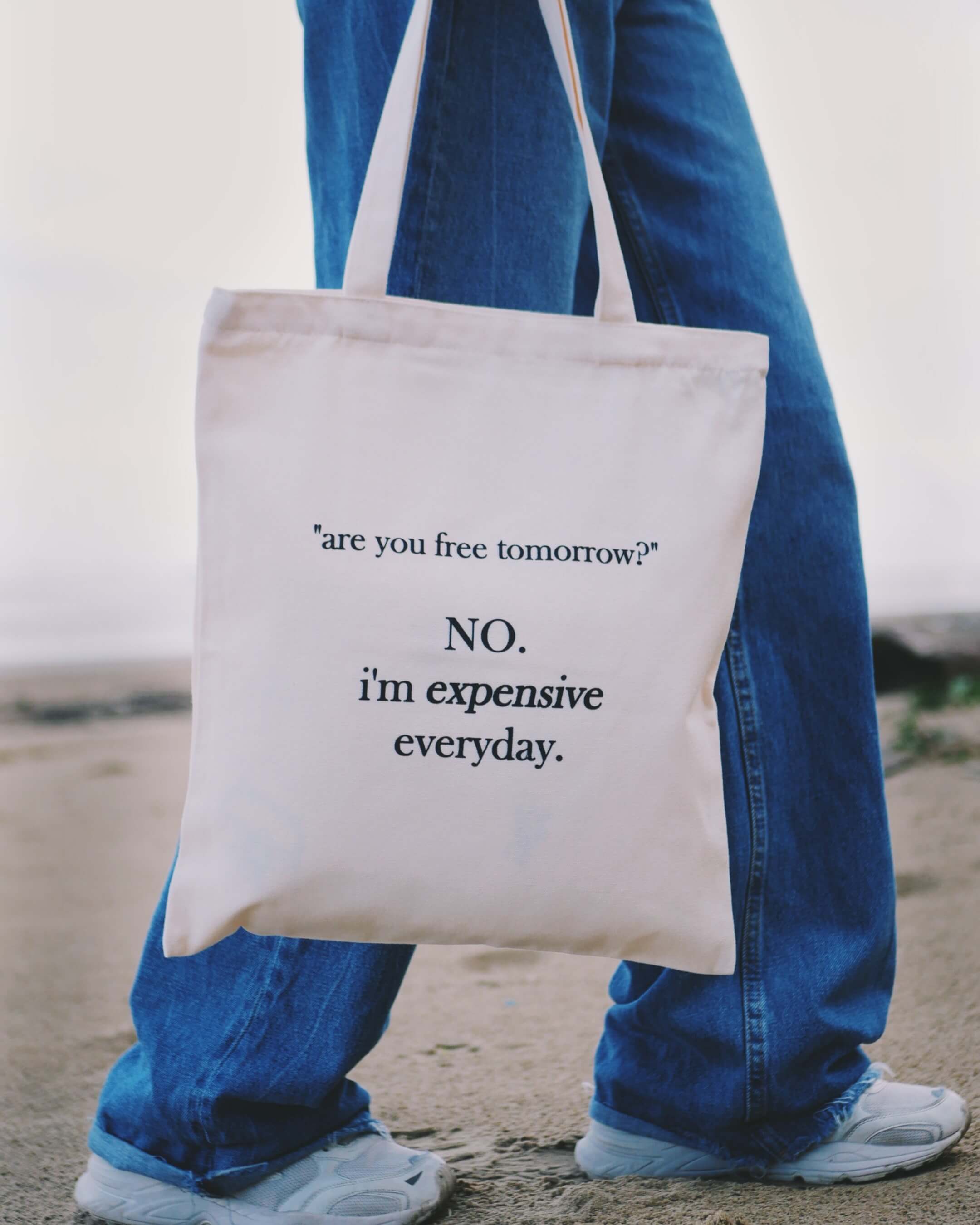 Person holding a tote bag with humorous text message on a beach.
